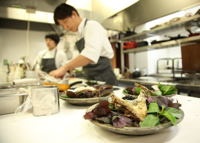 In the foreground, two prepared dishes, in the background, two chefs at Villa Aida, #35 on Asia's 50 Best Restaurants 2024.